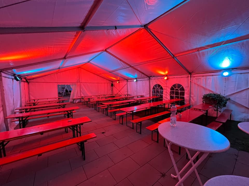 Festzelt mit Bierzeltgarnituren in rotem und blauem Licht