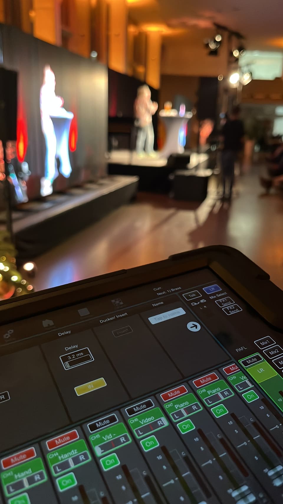 Tablet zur Mischpultsteuerung vor einer beleuchteten Bühne bei einer Saalveranstaltung